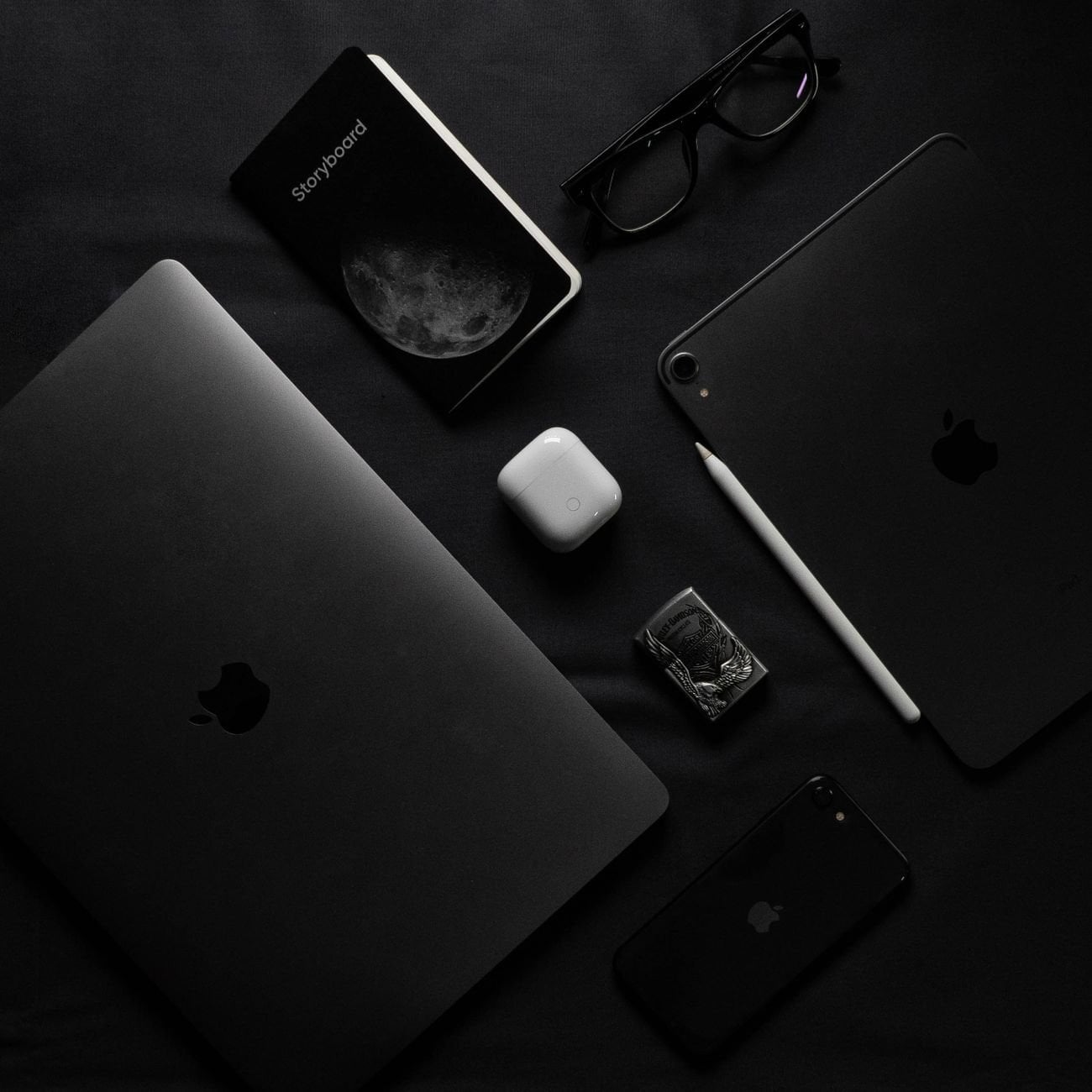 Dark minimalist flatlay of modern gadgets including laptop, smartphone, and eyeglasses
